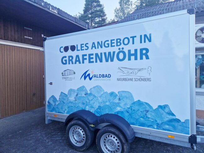 Seitenansicht des Kühlwagens der Stadt Grafenwöhr, beklebt mit einem Design, das Eisblöcke und Logos der Stadthalle, des Waldbads und der Naturbühne Schönberg zeigt